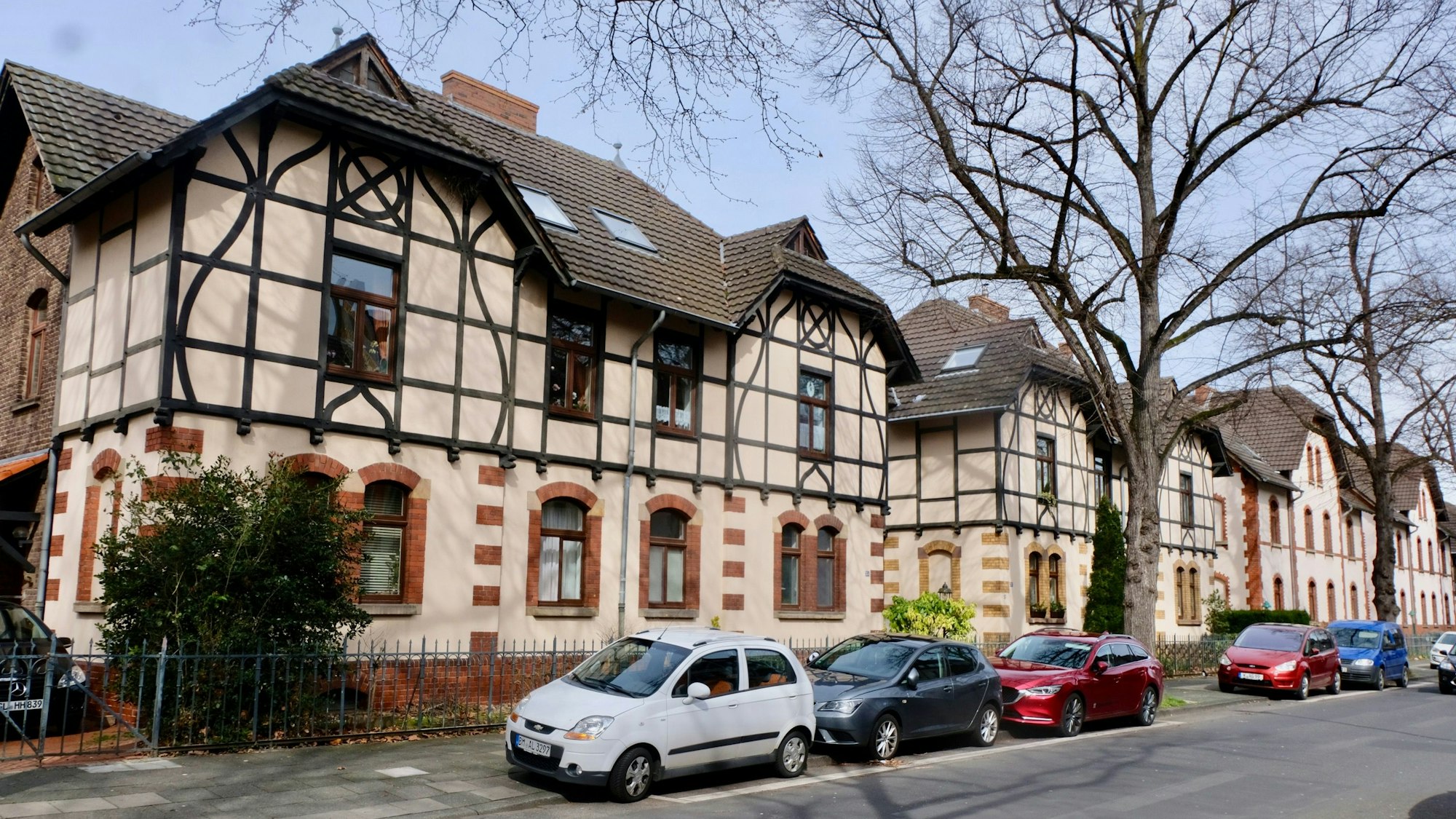Alte Häuser in Müngersdorf mit Autos, die auf der Straße davor parken.