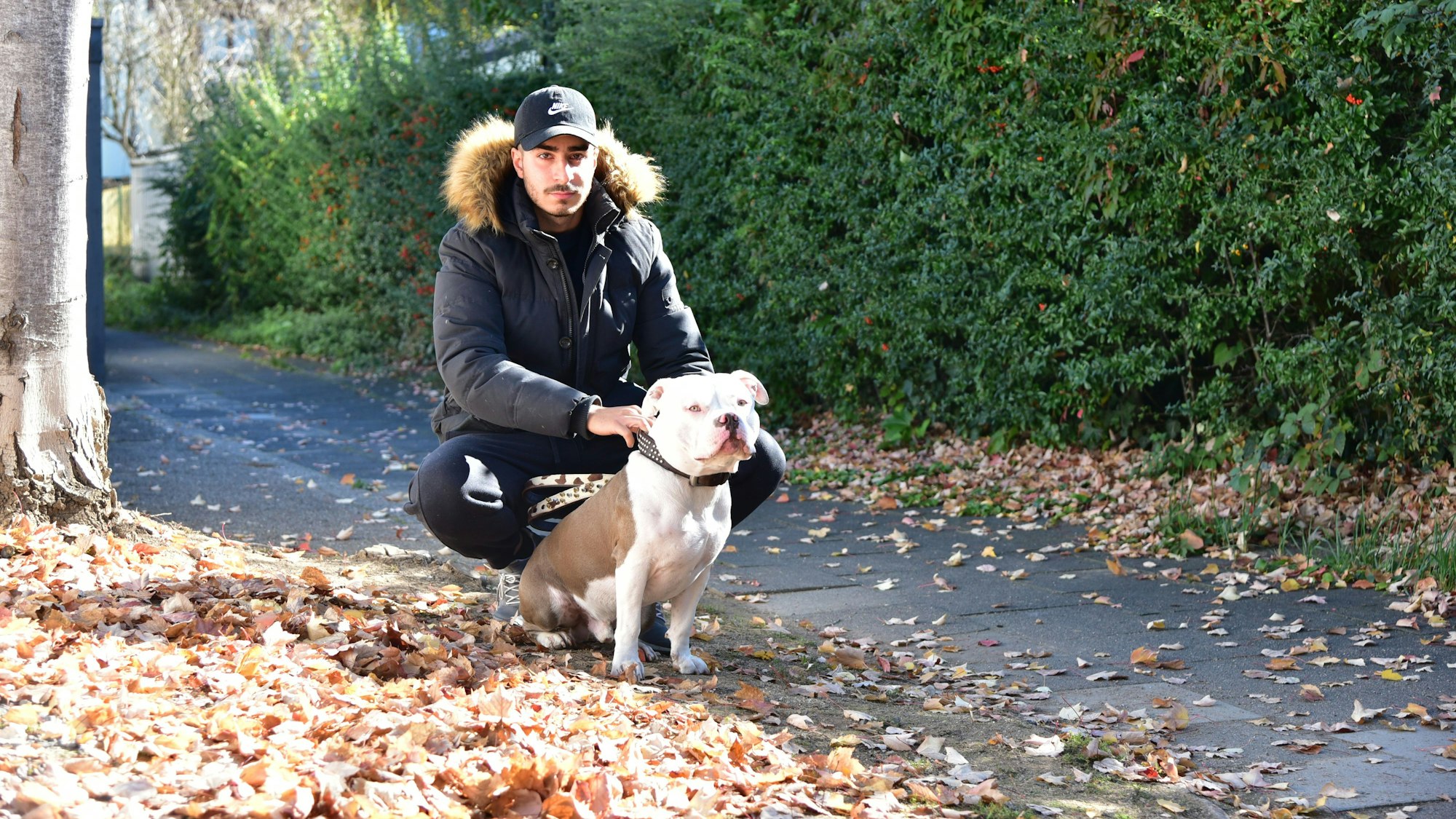 Onur C. und sein Hund Bonez hocken auf dem Bürgersteig neben einem Baum.