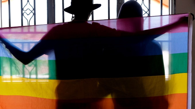 Ein schwules ugandisches Paar bedeckt sich mit einer Pride Flagge, während sie für ein Foto in Uganda posieren.