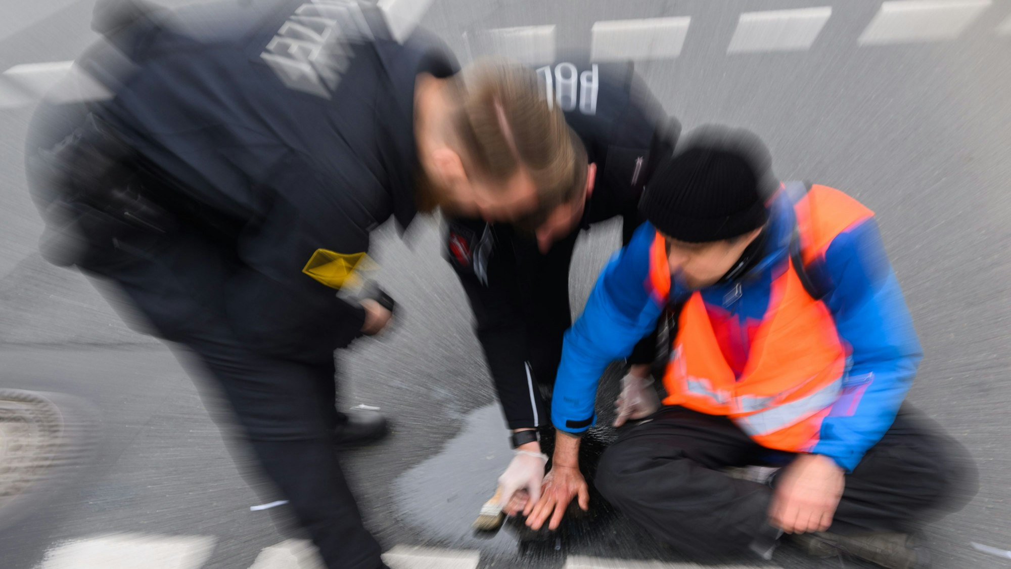 Ein Polizist versucht, festgeklebte Hände von Aktivisten der Gruppierung Letzte Generation von der Straße abzulösen.