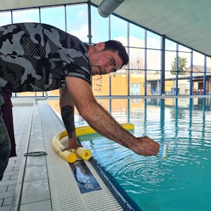 Das Bild zeigt einen Mann, der im Schwimmbad einen Wasserprobe nimmt.