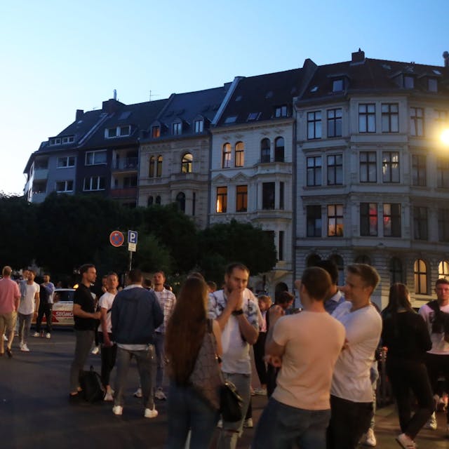Menschen stehen an einem Sommerabend am Brüsseler Platz.
