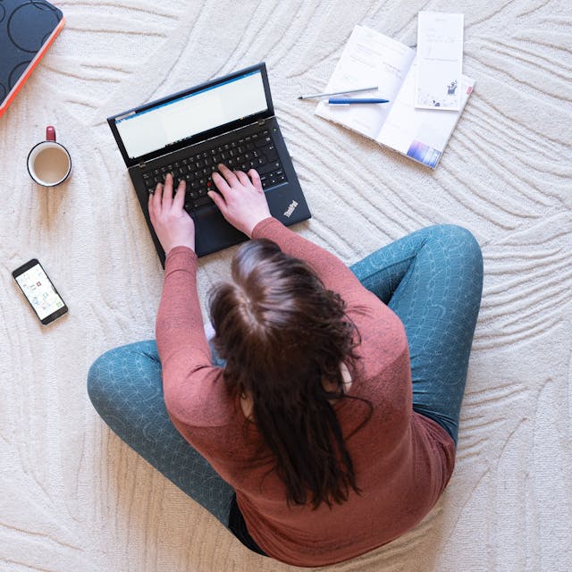Eine Frau sitzt im Homeoffice auf einem Teppich und arbeitet an einem Laptop (Symbolbild).