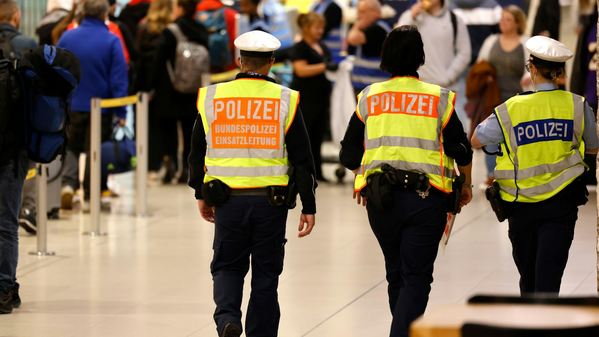 Zu sehen sind drei Bundespolizisten in der Rückansicht, die am Flughafen Köln/Bonn patrouillieren.