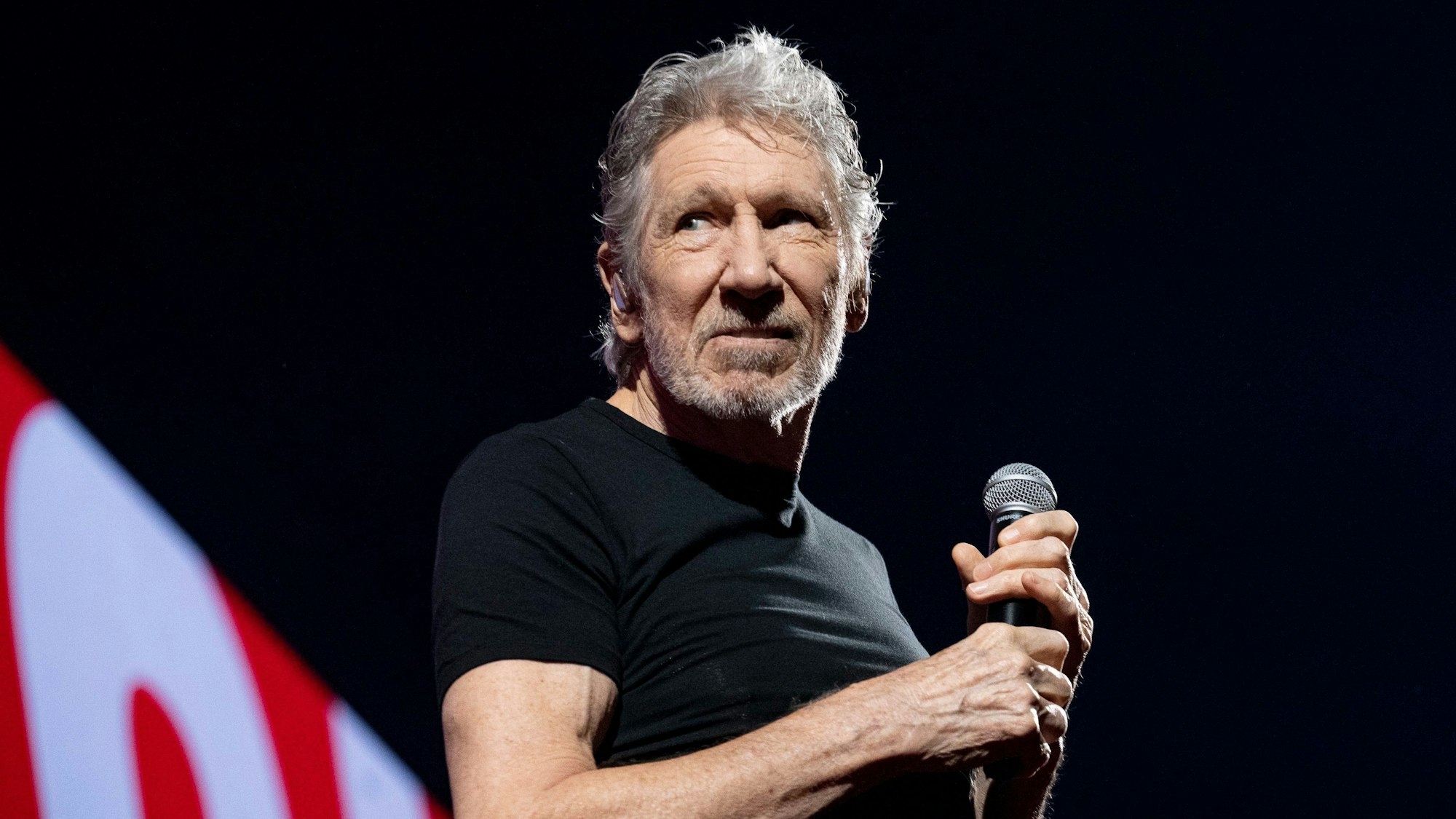 Roger Waters steht auf der Bühne und schaut zur Seite.