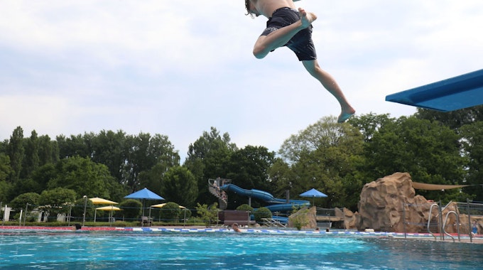 Ein junger Mann springt mit ausgestreckten Armen von einem Sprungbrett ins Bad Honnefer Freibad, Im Hintergrund ist die große blaue Wasserrutsche zu sehen.
