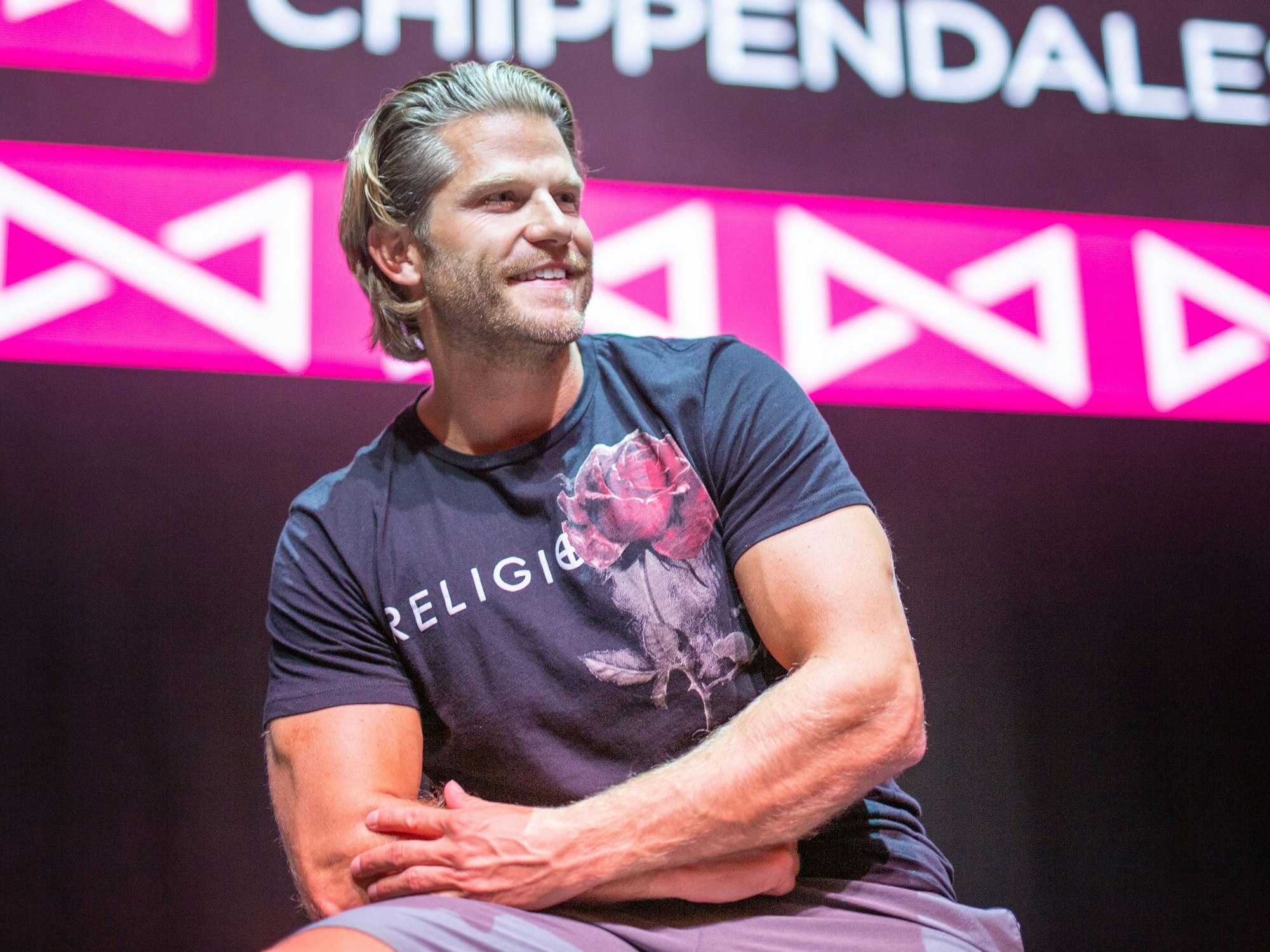 Paul Janke, Ex-„Bachelor“, sitzt vor dem Logo der Tanzgruppe Chippendales.
