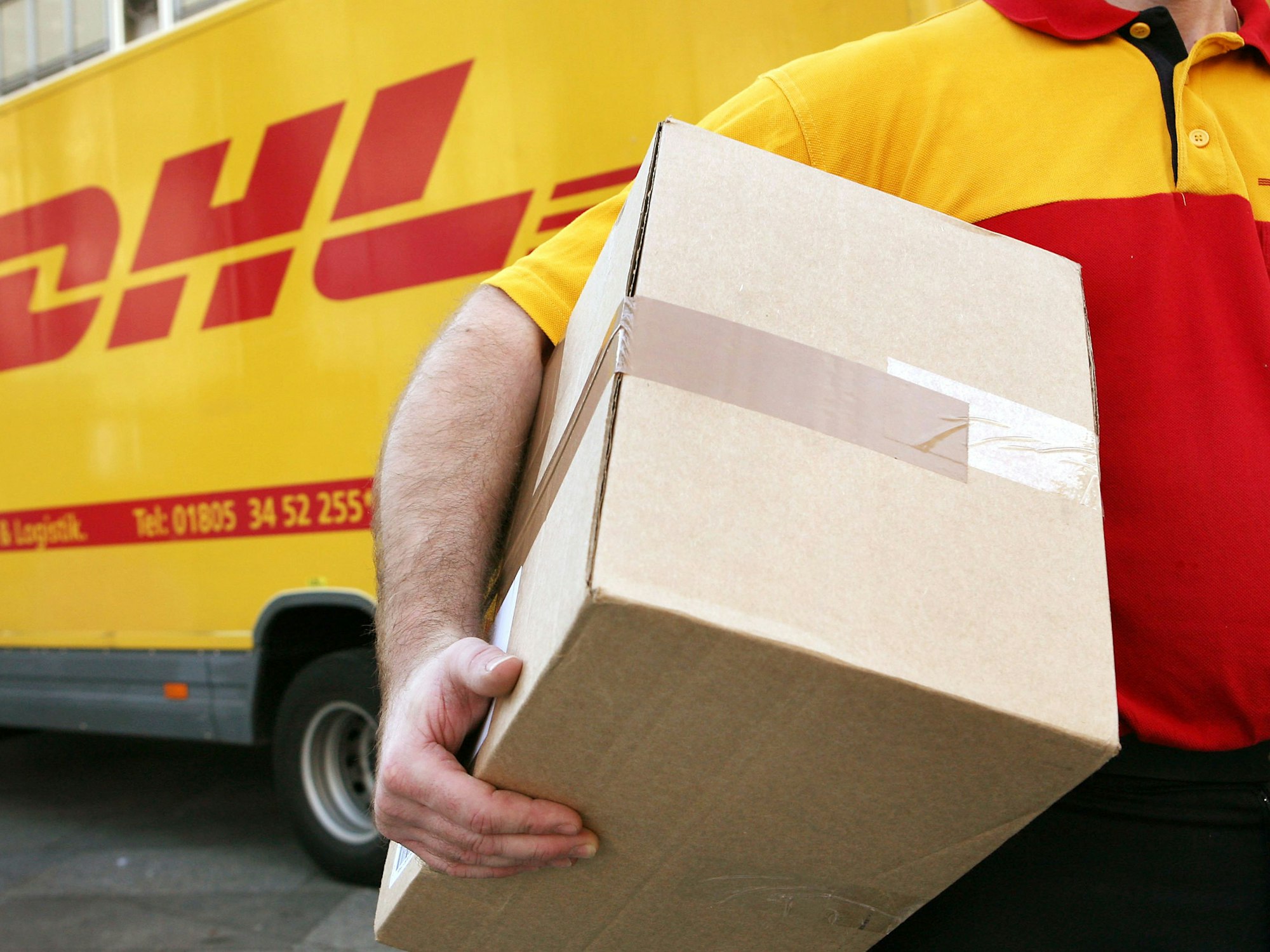 Ein Mitarbeiter des Paketdienstleisters DHL der Deutschen Post trägt ein Paket zum Kunden.