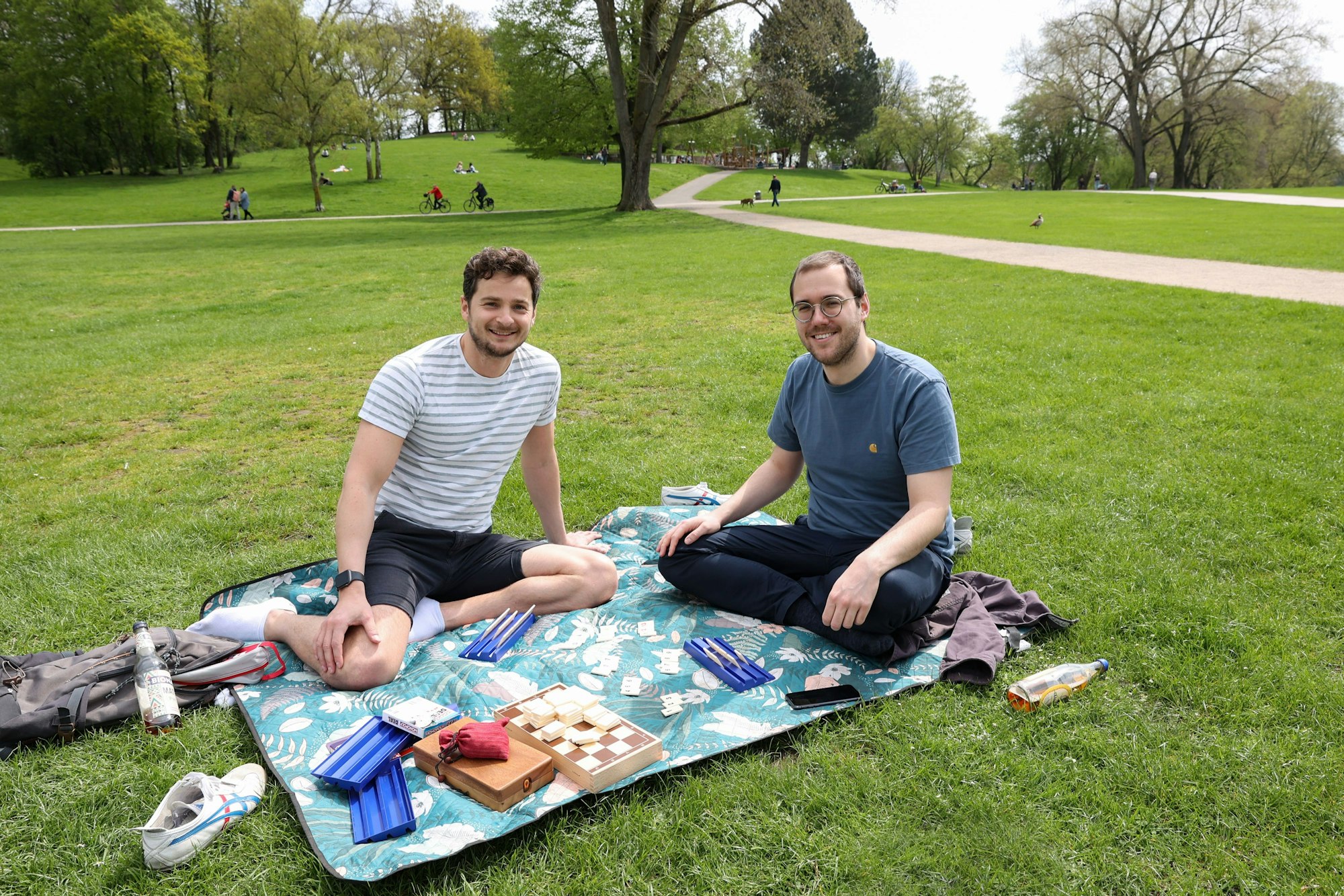 Arseni und David sitzen im Park auf einer Picknickdecke.