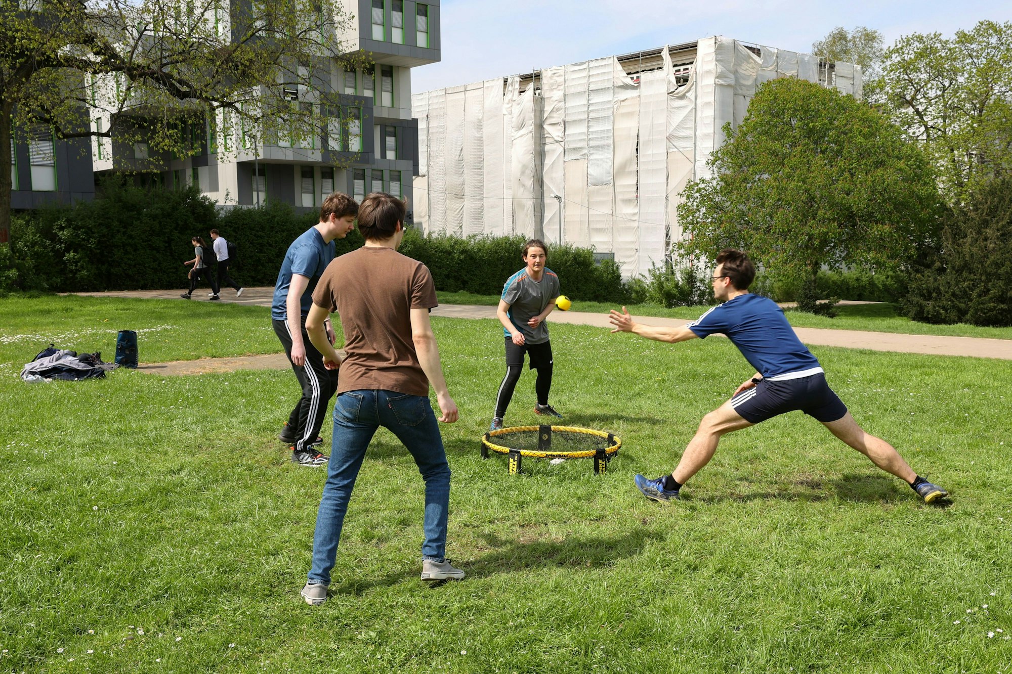 Sam, Niklas, Walter und Ellis spielen Spikeball auf einem grünen Rasen.