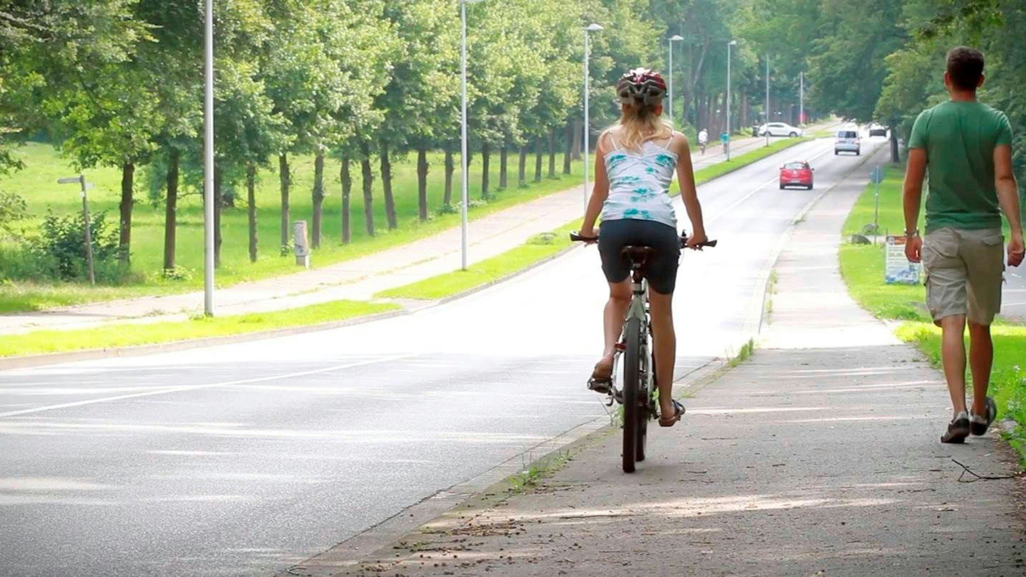 Mit dem Rad sicher durch den Straßenverkehr. Eine Radfahrerin und ein Fußgänger zeigen wie Konflikte vermieden werden können