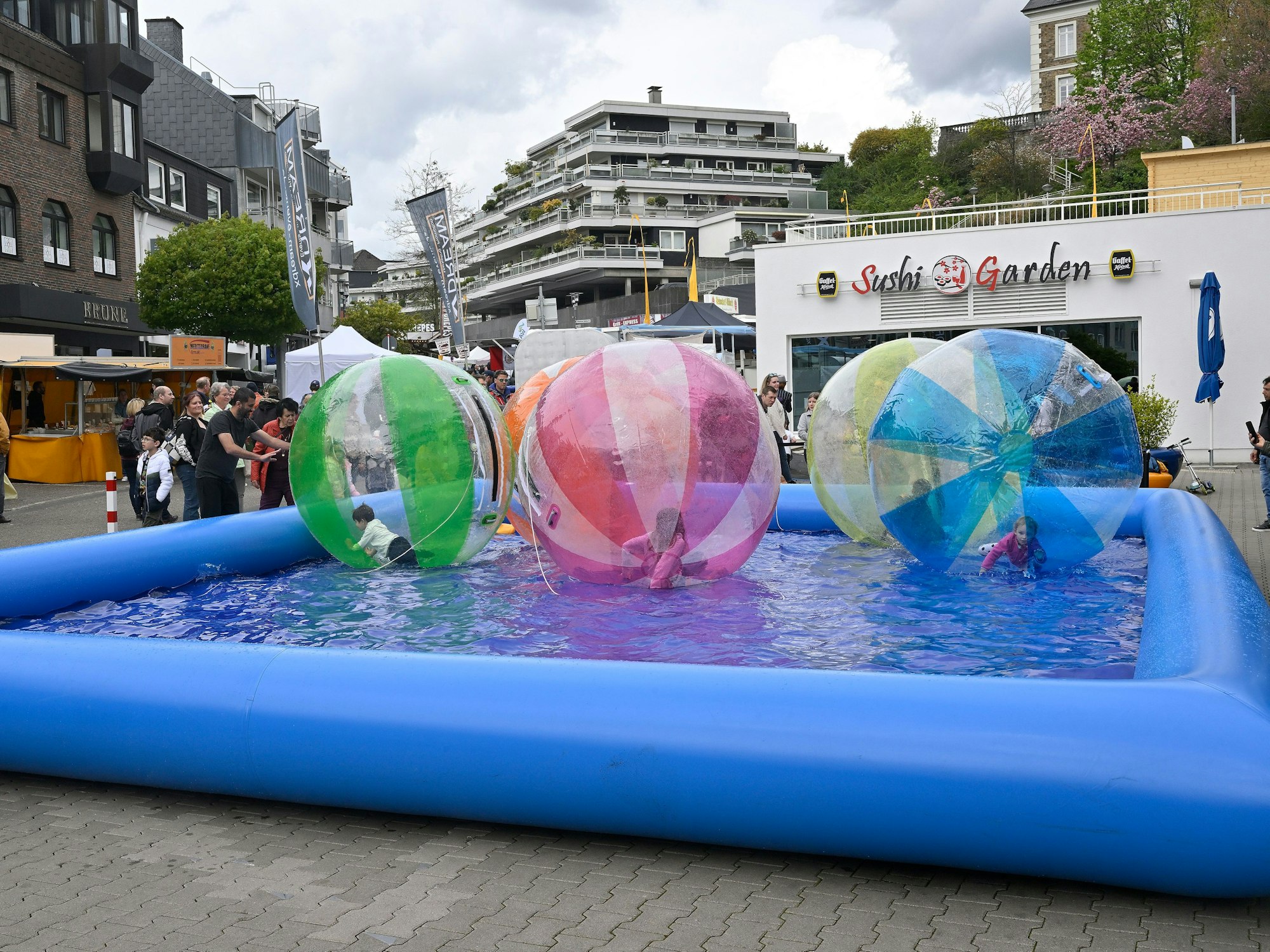 Kinder spielen in großen Wasserbällen in einem Pool in der Fußgängerzone.