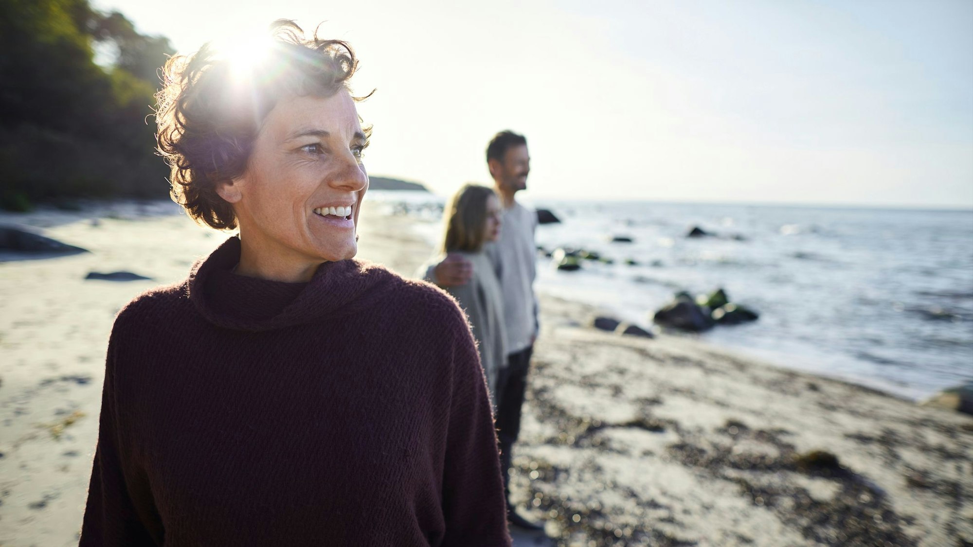 Smiling woman on the beach with family in background, Foto: Getty Images/Oliver Rossi