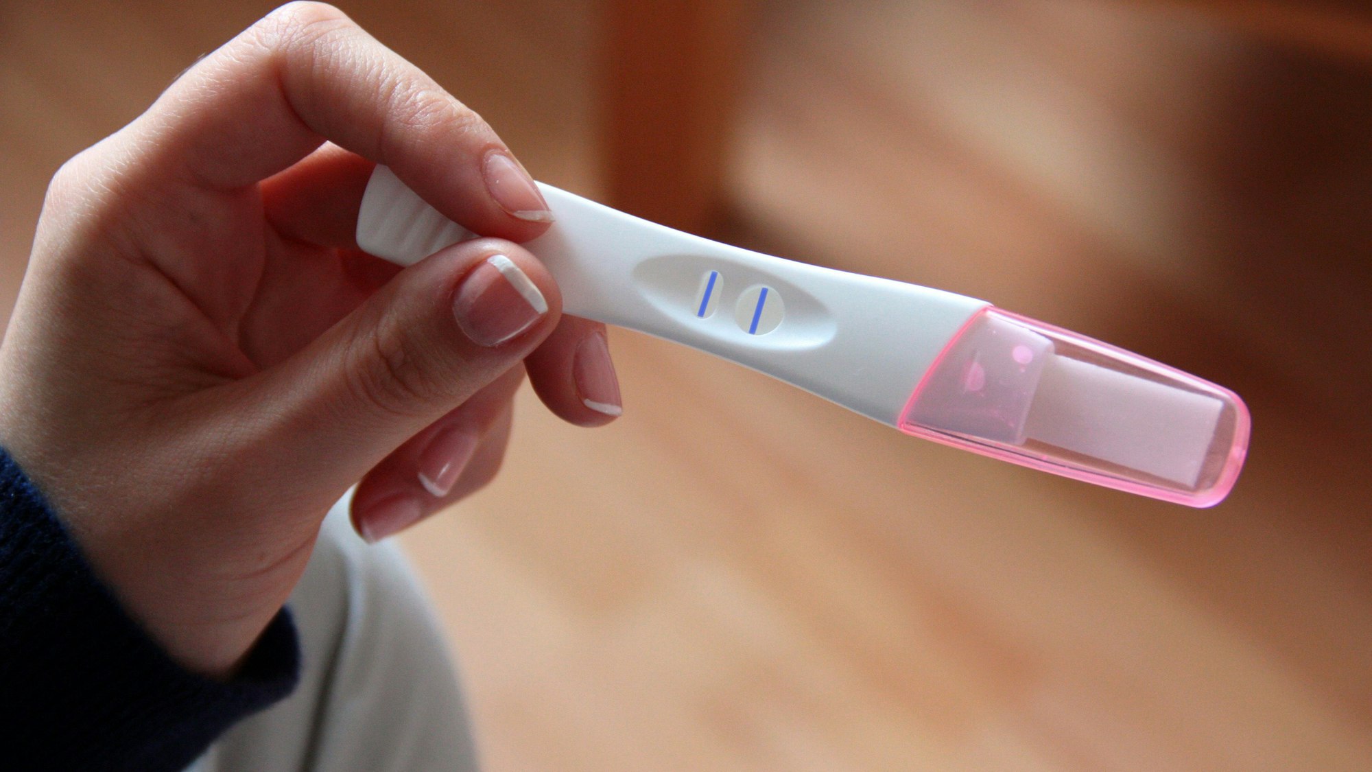 Eine Frau hält einen positiven Schwangerschaftstest in der Hand.