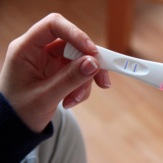 Eine Frau hält einen positiven Schwangerschaftstest in der Hand.
