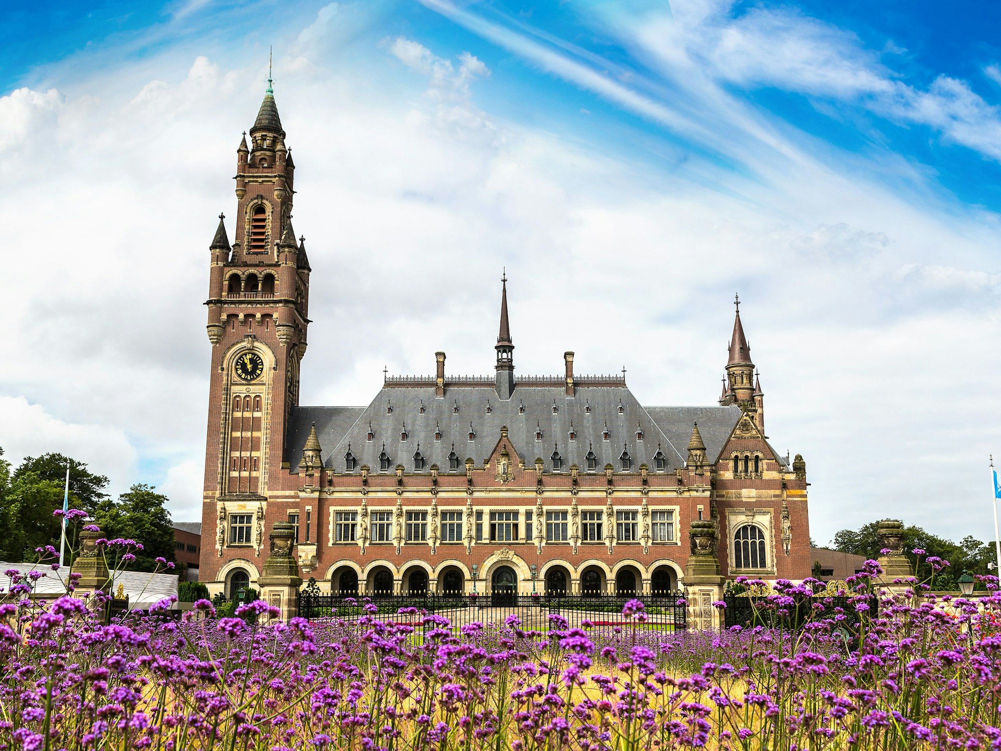 Das Foto zeigt den Friedenspalast in Den Haag, im Vordergrund stehen Blumen.