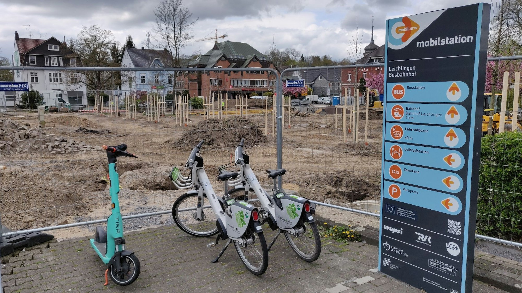 Zwei Leihräder und ein Roller stehen an der eingezäunten Mobilstation neben der Baustelle am Stadtpark Leichlingen