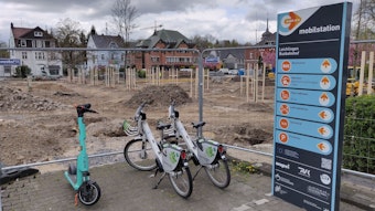 Zwei Leihräder und ein Roller stehen an der eingezäunten Mobilstation neben der Baustelle am Stadtpark Leichlingen