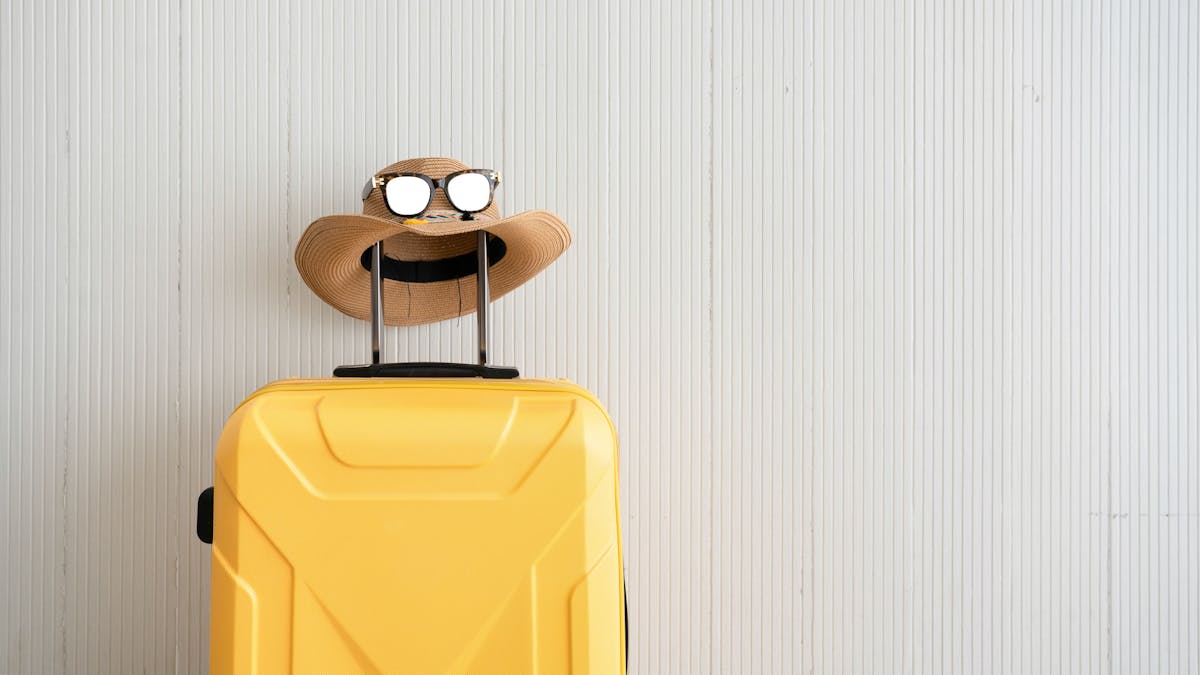 Ein gelber Koffer samt Strohhut und Sonnenbrille stehr abreisebereit parat.