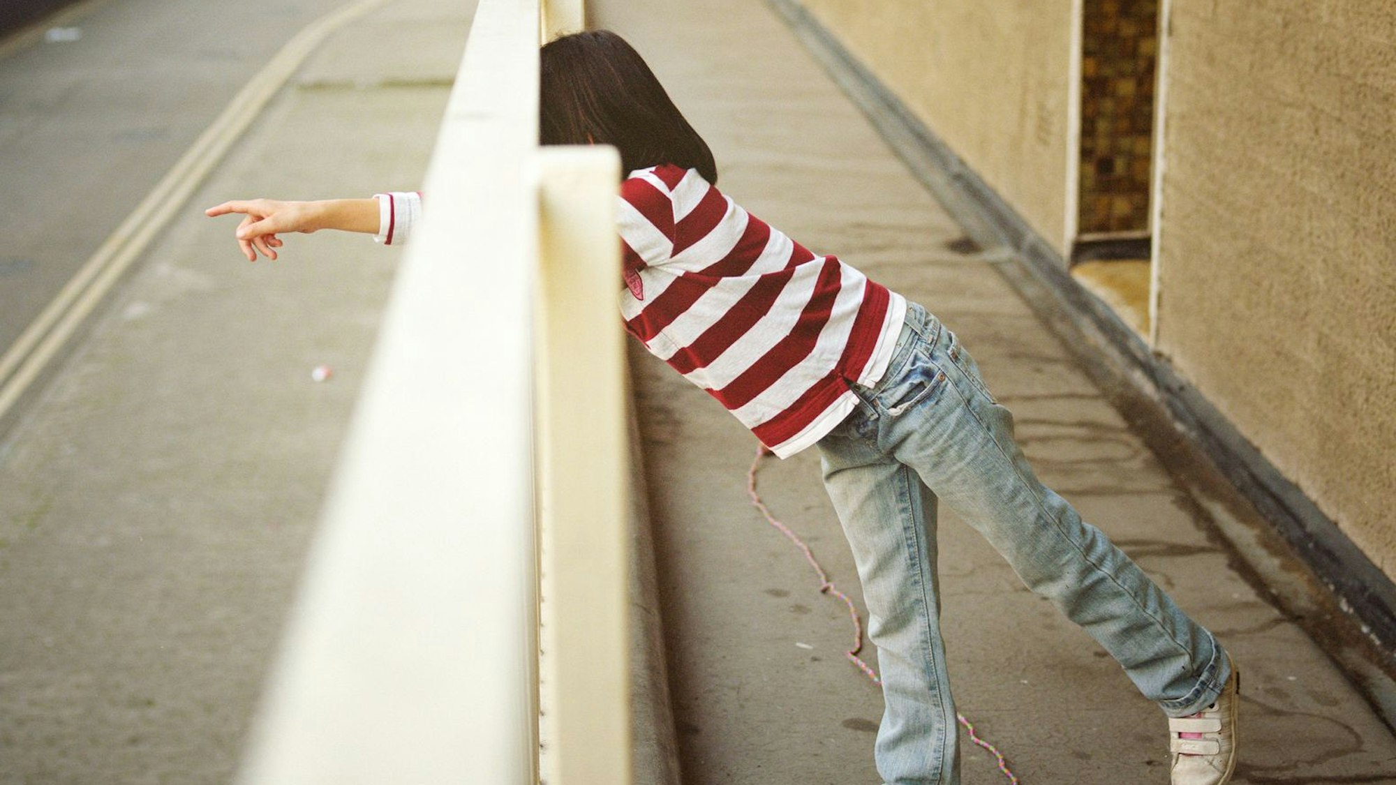 Ein junges Mädchen in einem rot-weiß gestreiften T-Shirt streckt ihren Arm sehnsüchtig durch ein Gatter.