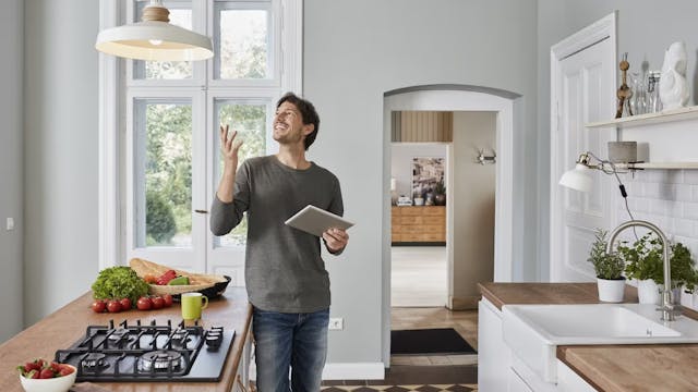Glücklicher Mann nutzt Tablet in Küche und guckt auf Lampe an der Decke.