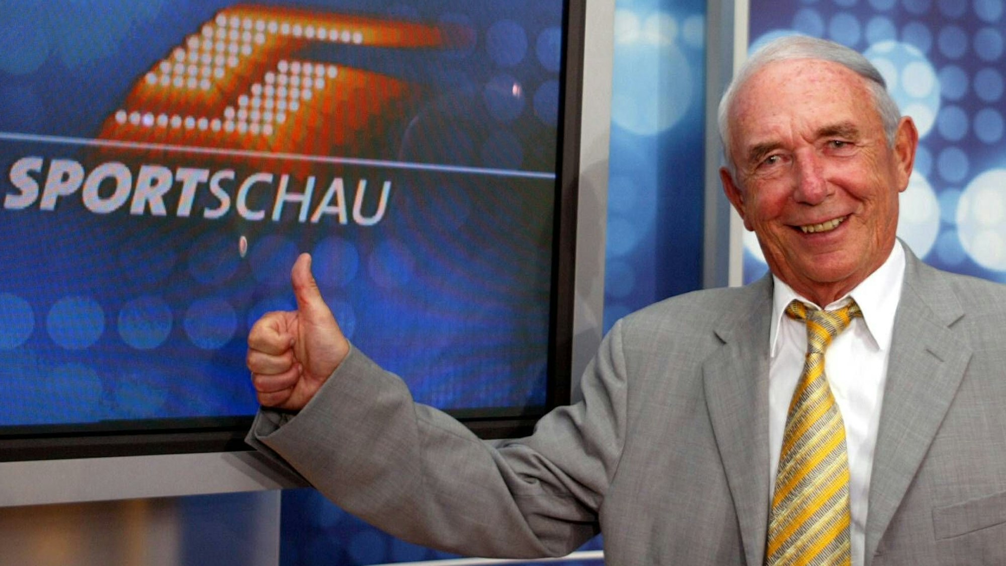 Das Bild zeigt Ex-Sportschau Moderator Ernst Huberty, vor dem Logo der Sportschau.