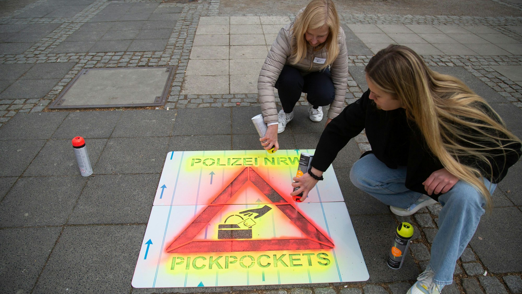Mit Sprühkreide bringen Polizistinnen am Neumarkt in Köln Warnungen vor Taschendieben an.