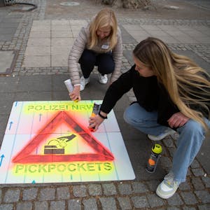 Mit Sprühkreide bringen Polizistinnen am Neumarkt in Köln Warnungen vor Taschendieben an.