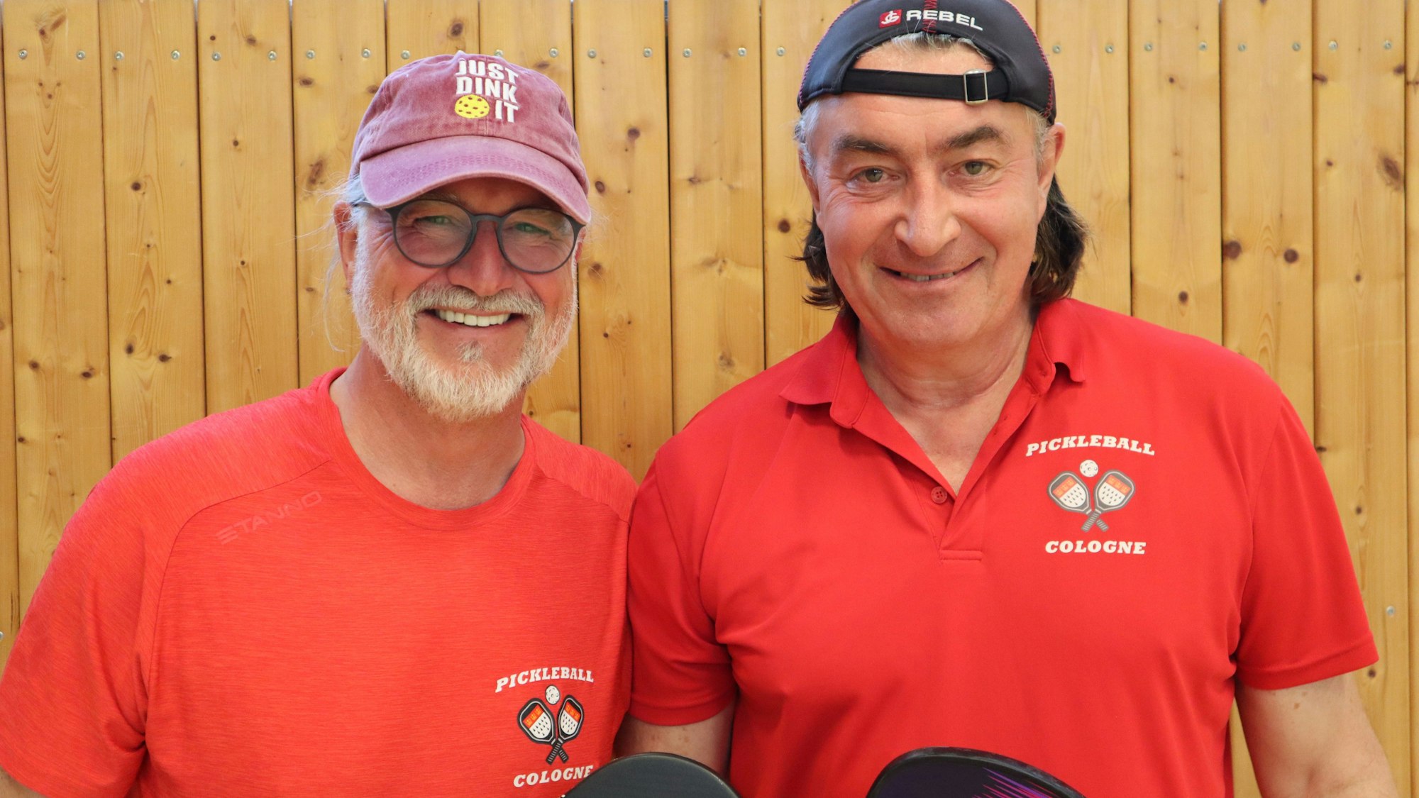 Zwei Männer mit rotem T-Shirt mit der Aufschrift „Pickleball Cologne“ und Kappen