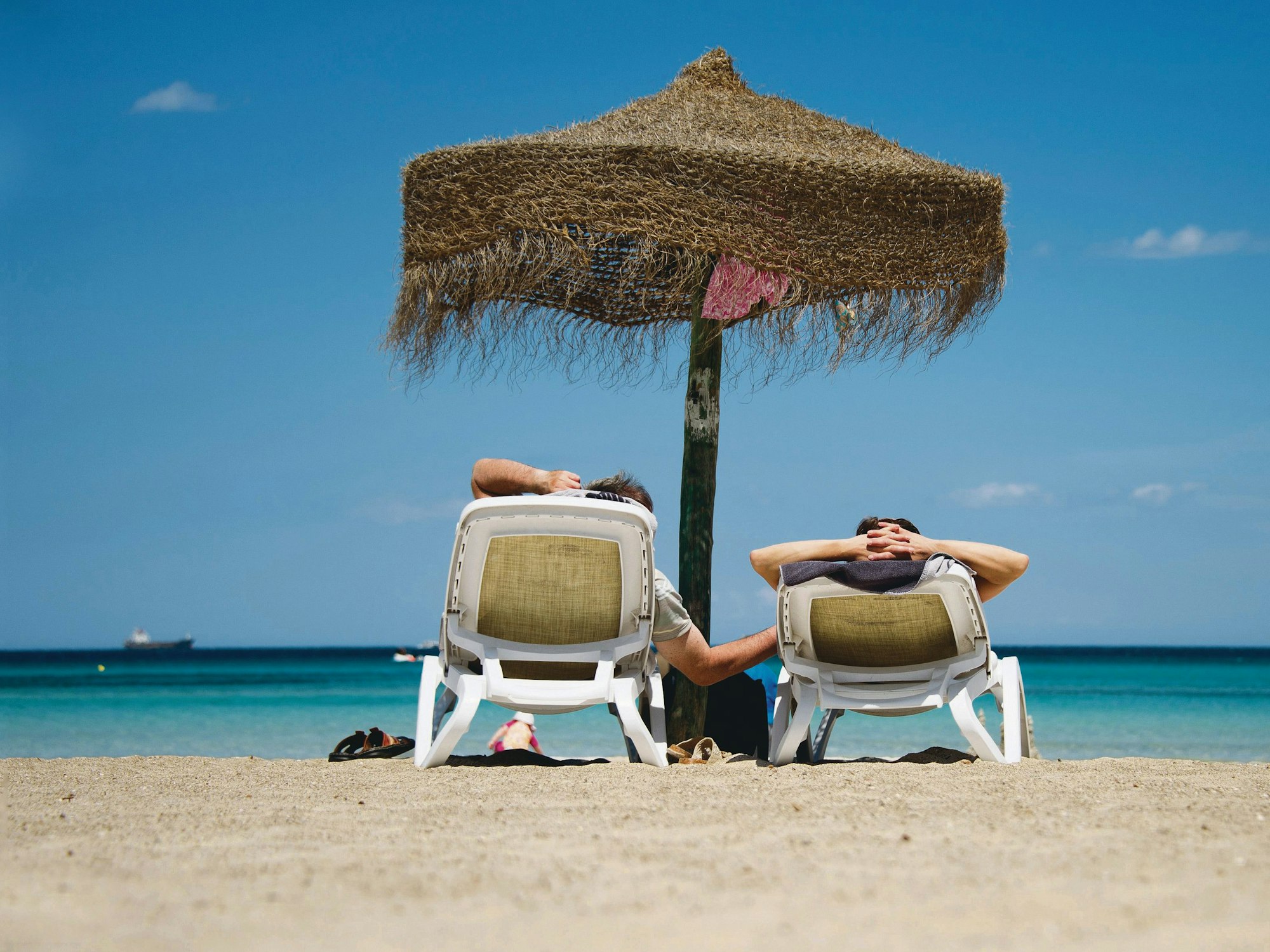 Zwei Urlauber auf Liegen unter einem Sonnenschirm an derPlaja de Muro auf Mallorca.