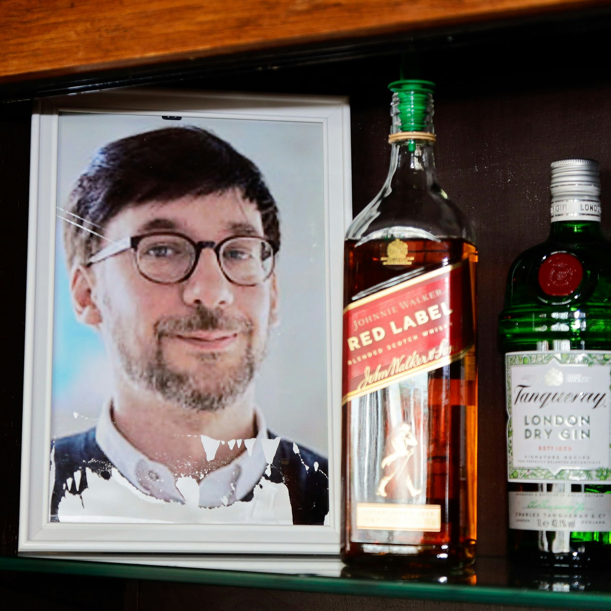 Ein gerahmtes Foto steht in einem Regal neben Alkoholflaschen.