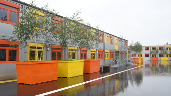 Containerbauten mit orangen und gelben Fenstern und bunten Pflanzkübeln.&nbsp;
