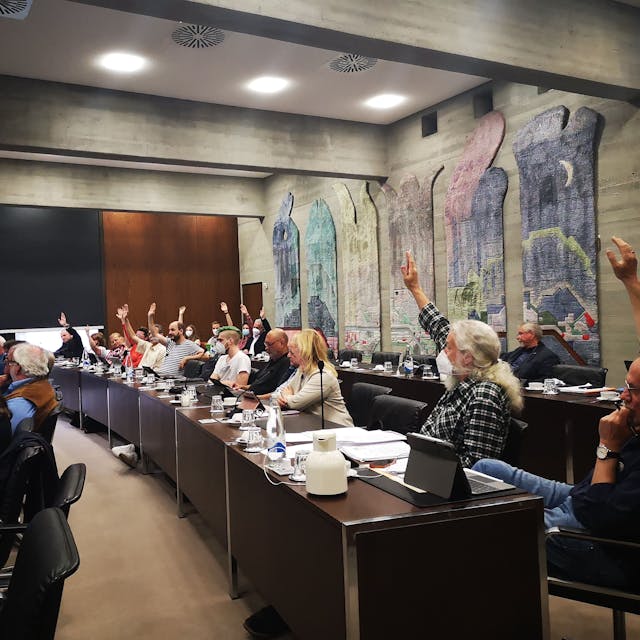 Die Ratsmitglieder in Wesseling stimmen im Ratssaal über Beschlüsse ab. Die Menschen sitzen an langen Tischen und heben teilweise ihrer Hand zur Abstimmung.