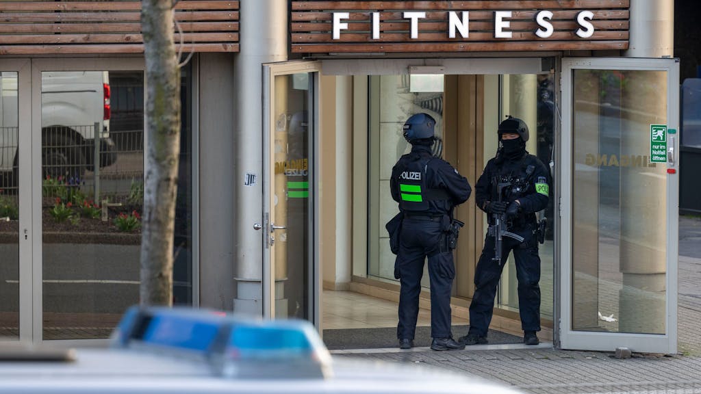 Das Foto vom 18. April 2023 zeigt zwei Polizisten, die im Eingang eines Fitnessstudios stehen. Im Vordergrund befindet sich ein Einsatzwagen der Polizei.&nbsp;
