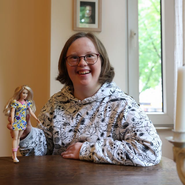 Die Kölnerin Natalie Dedreux lacht in die Kamera und hält die neue Barbie mit Down-Syndrom in ihrer rechten Hand.&nbsp;