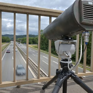 Eine Monocam zur Aufzeichnung von Handysündern am Steuer steht auf einer Brücke über einer Autobahn.