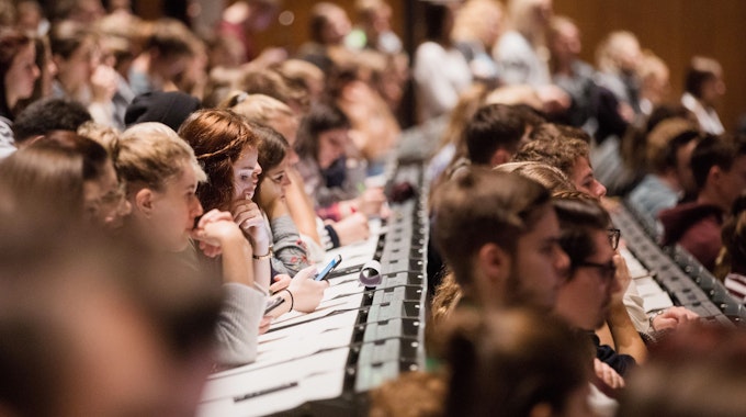 Studenten und Studentinnen verfolgen sitzen in einem Hörsaal.