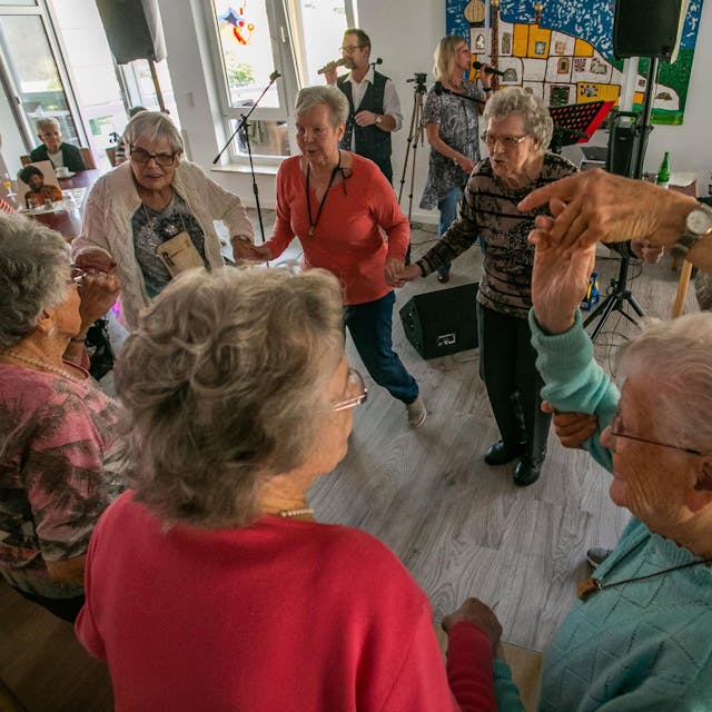 Senioren und Seniorinnen tanzen zu Schlagermusik in einem Partyraum.
