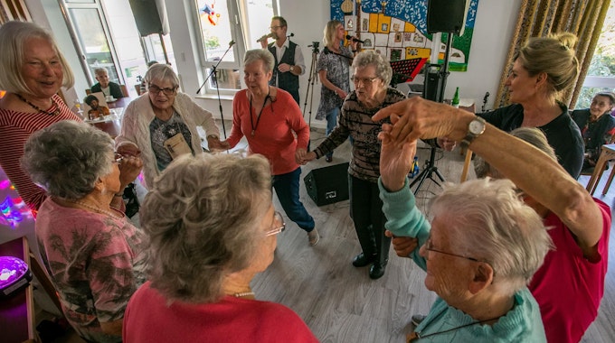 Senioren und Seniorinnen tanzen zu Schlagermusik in einem Partyraum.