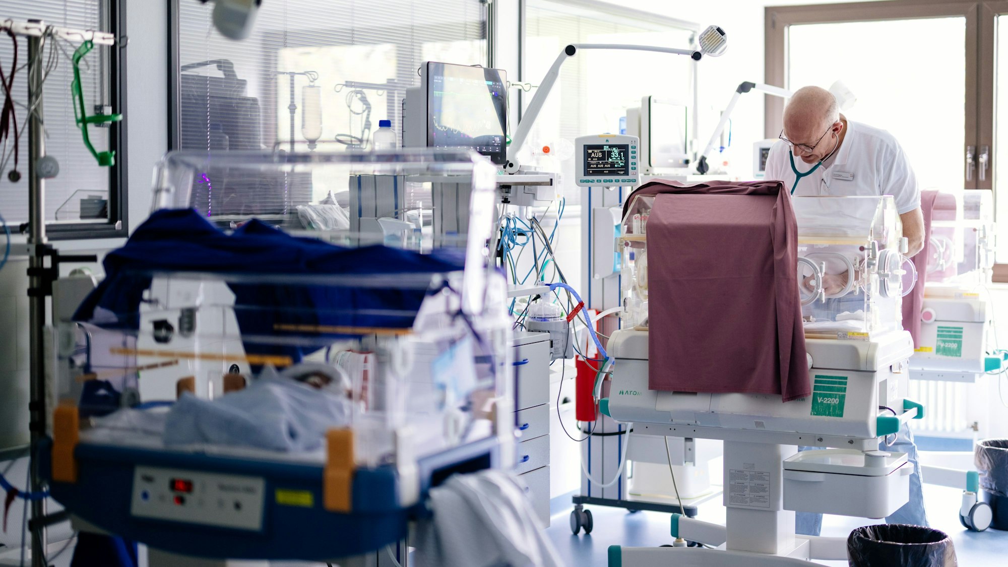 In den Brutkästen, den sogenannten Inkubatoren, herrscht dank darüber gelegter roten Tüchern dämmeriges Licht wie im Mutterleib. Ein Arzt untersucht ein Kind darin.