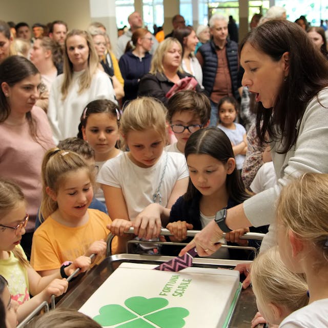 Von Kindern umringt schnitt Rektorin Britta Bockschewsky bei der Eröffnungsfeier der Oberaußemer Fortunaschule eine mit dem Kleeblatt-Logo verzierte Torte an.