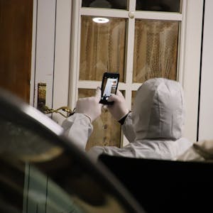 Eine Person im Schutzanzug fotografiert eine Fensterscheibe.