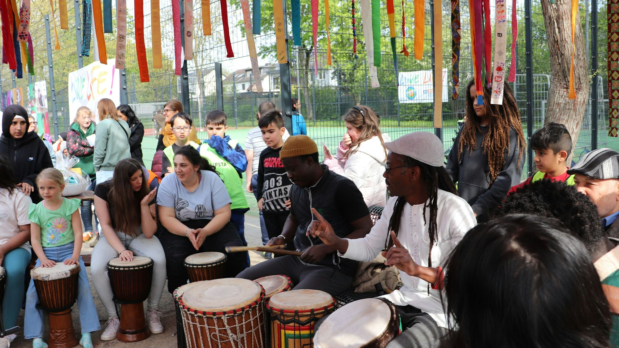Die Band Mama Afrika trommelt gemeinsam mit Kindern und Jugendlichen unter einem bunt geschmückten Baum.