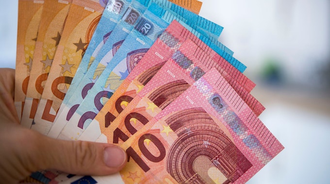 Eine Person hält Banknoten von 10, 20 und 50 Euro gefächert in der Hand.