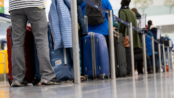 Passagiere stehen mit ihrem Gepäck an Check-in-Schaltern am Flughafen. 