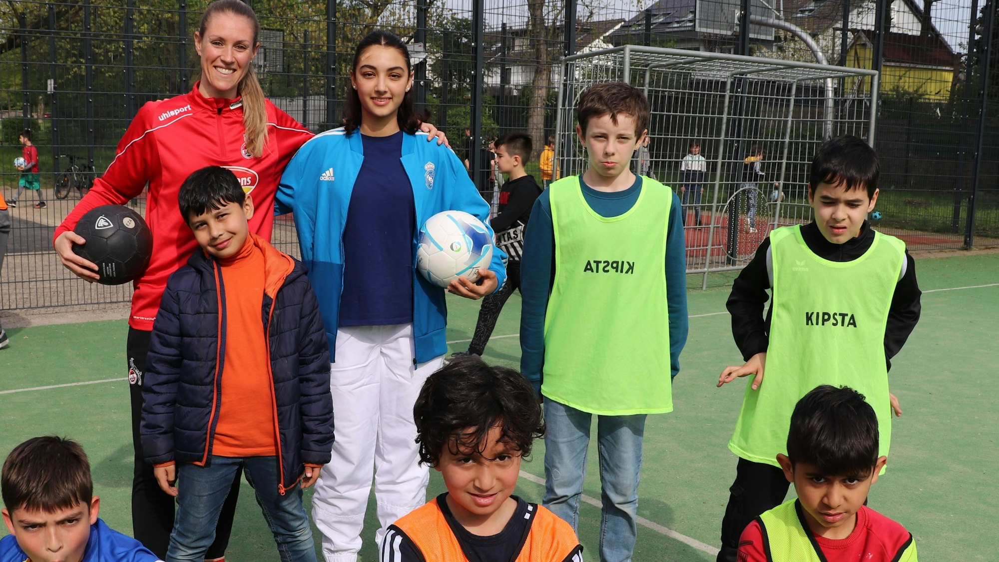 Ex-FC Profispielerin Nina Windmüller steht vor einem Fußballtor umgeben von Kindern in bunten Trikots.