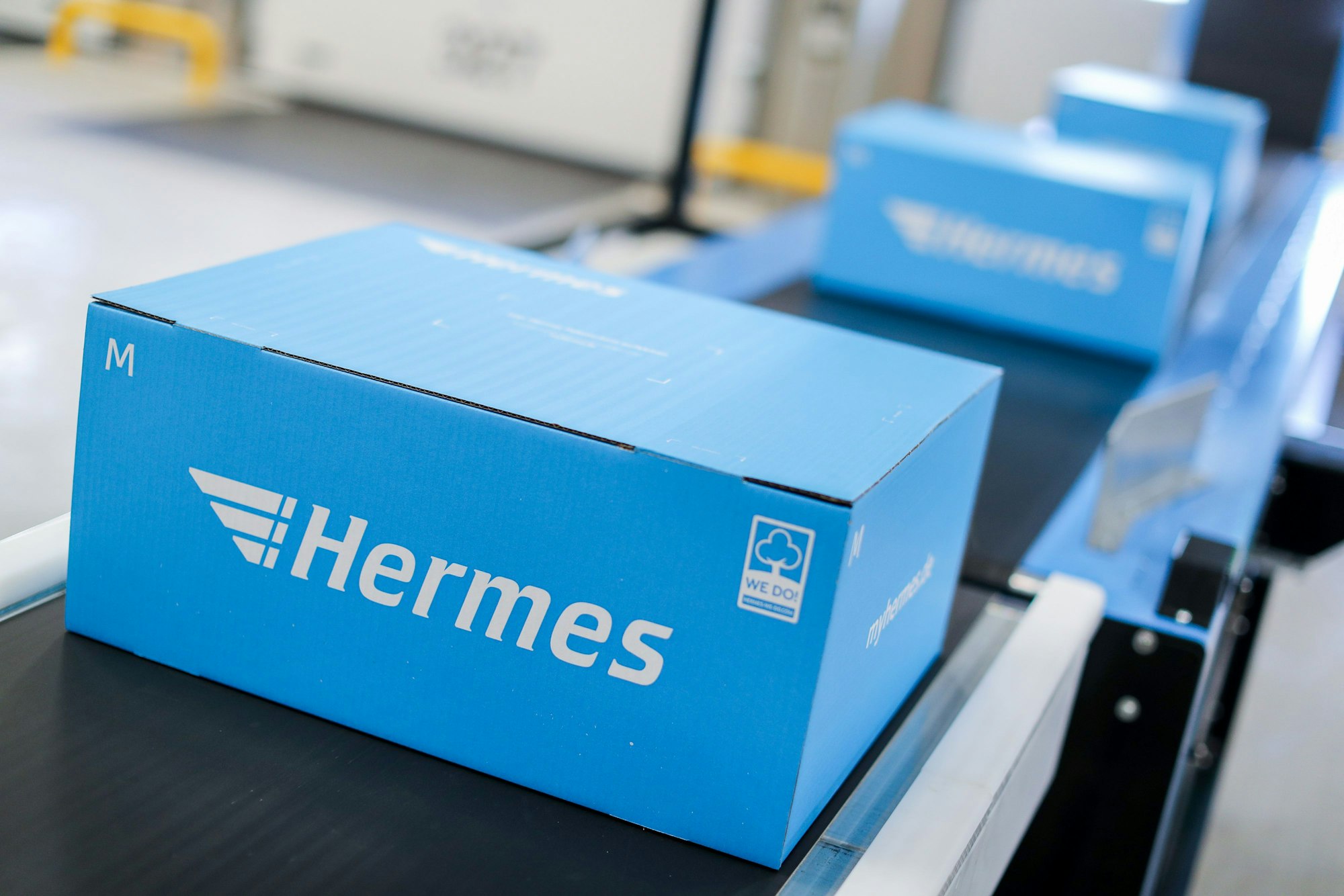 Blaue Pakete liegen auf einem Förderband eines Hermes Logistik-Centers.