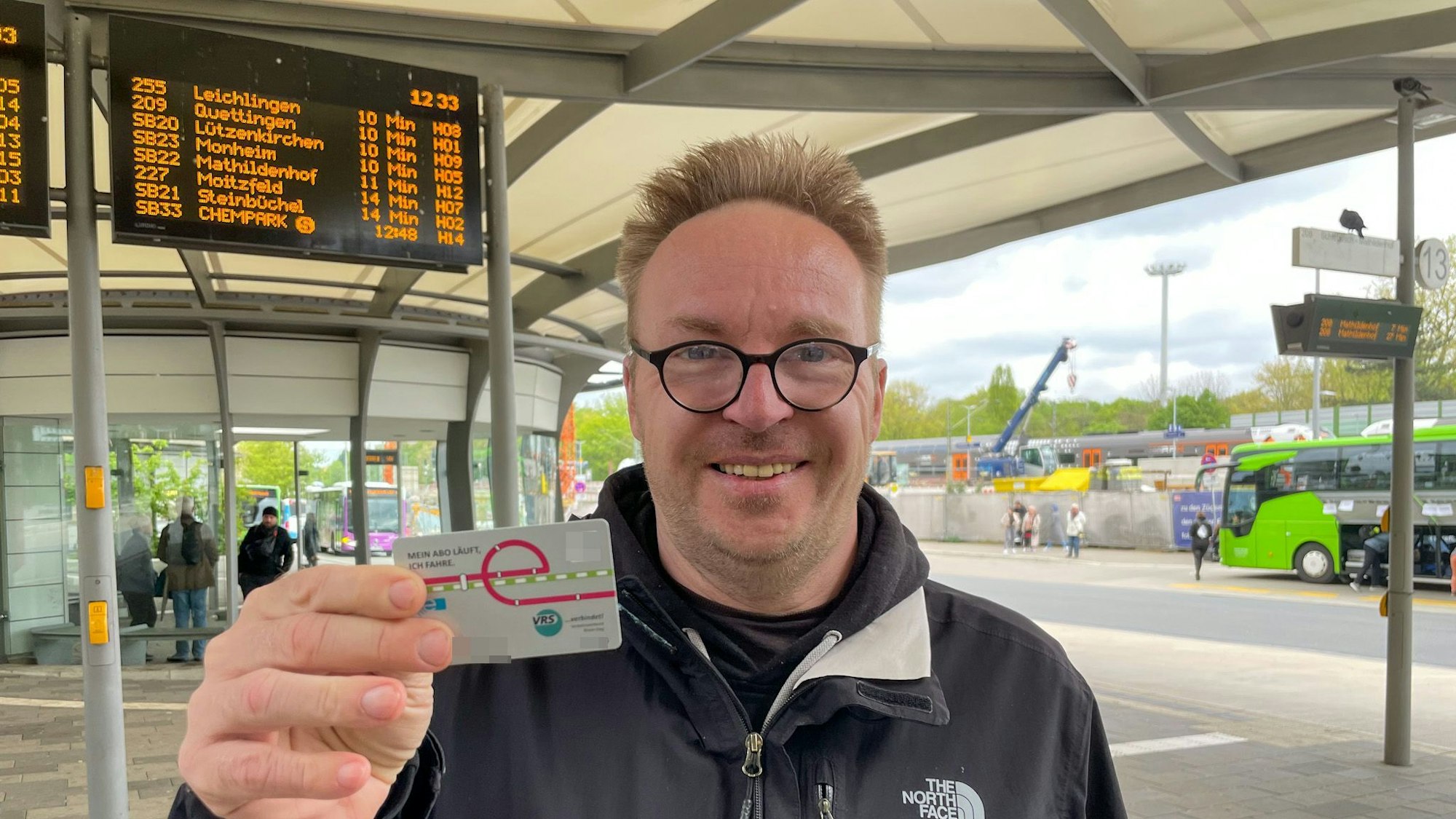 Christof Schmidt steht am Leverkusener Busbahnhof und hält sein Deutschlandticket vor sich.