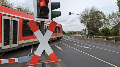 Ein Zug rollt hinter geschlossenen Schranken über den Bahnübergang an der Bonnstraße in Hürth-Fischenich.
