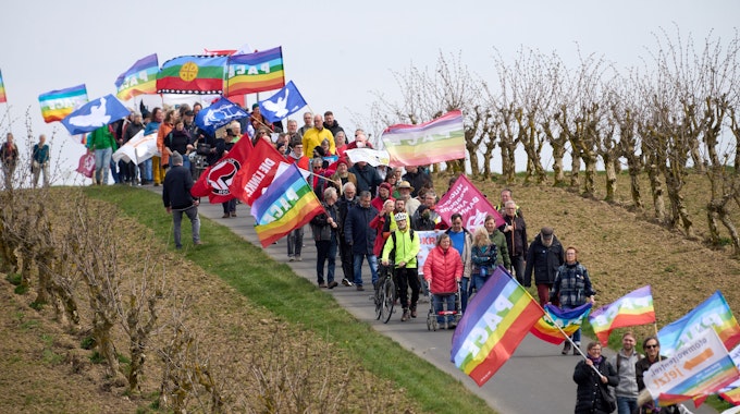 Teilnehmer des Ostermarsches laufen am Zaun des Bundeswehr-Fliegerhorsts mit bunten Flaggen vorbei.&nbsp;